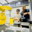 FANUC și WorldSkills au demarat o olimpiadă de integrare de roboți industriali Doi studenți din Cluj-Napoca vor reprezenta România la Olimpiada Europeană de Meserii EuroSkills 2023, secțiunea integrare de sisteme de roboți. FANUC și WorldSkills România au organizat prima ediție a Olimpiadei Naționale FANUC WorldSkills de Integrare de Roboți Industriali pentru tinerii români. Patru echipe de studenți de la universitățile tehnice din țară au concurat la Cluj-Napoca în 26-27 aprilie. Echipa câștigătoare va reprezenta România la categoria integrare de sisteme de roboți în cadrul Olimpiadei Europene de Meserii EuroSkills Gdansk 2023, organizate în Polonia, în septembrie. Începutul anului a fost unul solicitant pentru studenții departamentelor de robotică din cadrul a patru instituții e învățământ superior: Universitatea Tehnică Lucian Blaga din Sibiu, Universitatea Tehnică Gheorghe Asachi din Iași, Universitatea Politehnică din București și Universitatea Tehnică din Cluj-Napoca. Ei au participat la cursuri și probe de preselecție în vederea calificării la prima ediție a Olimpiadei Naționale FANUC WorldSkills de Integrare de Roboți Industriali, organizată în România în primăvară, la sediul FANUC România, de lângă Cluj-Napoca. Cele patru echipe finaliste, alcătuite fiecare din câte doi studenți și un cadru didactic îndrumător, s-au întrecut timp de două zile, în patru probe de concurs, desfășurate exclusiv în limba engleză, în a-și demonstra abilitățile și cunoștințele de programare și utilizare a roboților industriali. Concursul, organizat în parteneriat de câtre FANUC România și Fundația WorldSkills România, are ca obiectiv pe termen lung aprofundarea cunoștințelor, abilităților și experienței practice ale studenților din universitățile tehnice românești în programarea și integrarea roboților industriali în perspectiva dezvoltării unei cariere profesionale într-un domeniu de foarte mare actualitate. Echipa câștigătoare va fi înscrisă ca reprezentantă din partea României la proba de integrare de sisteme de roboți de la EuroSkills Gdansk 2023. Membrii echipei câștigătoare sunt studenți în anul IV la Universitatea Tehnică din Cluj-Napoca (UTCN), Facultatea de Inginerie Industrială, Robotică și Managementul Producției. ,,Sarcina principală de lucru din cadrul compeției era un proces preluat din industrie. Așadar, a implicat toate detaliile tehnice precum electronică, modelare layout în RoboGuide, programare, instalarea echipamentelor și altele. A fost o experință foarte bună, fiindcă am avut ocazia să punem în practică ceea ce am studiat la facultate. Fiindcă exercițiul pricipal al compentiției a fost unul realist și ne-am aflat permanent sub presiunea timpului, consider că ne va ajuta enorm de mult în cariera noastră de roboticieni”, a spus Kántor Jozsue, membru al echipei câștigătoare. ,,Cel mai dificil a fost să lucrăm după standardele europene, enorm de stricte din toate punctele de vedere. Multitudinea de cerințe a generat o colaborare bună între noi. Fără lucrul în echipă nu am fi reușit o asemenea performanță”. a menționat Krasznai Györk Attila, celălalt membru al echipei câștigătoare. Aflându-se la prima ediție, experții români și organizatorii au primit sprijinul expertului britanic de origine română în integrare de sisteme de roboți Karla Kosch. Ea a participat la Olimpiadă în calitate de președinte al juriului. ,,Prima Olimpiada Națională de Integrare de Roboți Industriali desfășurată la Cluj-Napoca a dezvăluit talente din patru mari universități. Munca depusă cu dedicație de echipele de studenți din Cluj, București, Sibiu și Iași a fost cu atât mai evidentă cu cât concursul a fost susținut în limba engleză. E un pas îndrăzneț și lăudabil care aduce România cu un pas mai aproape de competițiile internaționale. Felicitări organizatorilor - FANUC România și WorldSkills România - pentru această inițiativă unica și mult succes la EuroSkills Gdansk în septembrie 2023”, a spus Karla Kosch, lector în inginerie la Northern Regional College, Irlanda de Nord. În timp ce automatizarea industrială și robotizarea au devenit soluții preferate de producătorii industriali pentru sporirea competitivității și a performanței, multe companii se confruntă cu o criză a lucrătorilor calificați. Prin astfel de parteneriate și implicarea în proiecte educaționale, FANUC oferă oportunități noilor generații în a învăța tot mai mult și a se specializa în domeniile de interes. Corporația FANUC este unul dintre liderii mondiali în automatizarea fabricilor pentru sisteme de control CNC, roboți și mașini de producție (Robodrill, Robocut și Roboshot). Din 1956, este pionier în dezvoltarea mașinilor cu comandă numerică în industria automatizării. Cu 266 de locații FANUC în întreaga lume și 8.000 de angajați, FANUC oferă o rețea densă de vânzări, suport tehnic, cercetare și dezvoltare, logistică și servicii pentru clienți. FANUC România este subsidiara locală a organizației FANUC și are sediul principal în Cluj-Napoca. Din 2018, FANUC, în calitate de producător de top de roboți industriali, a devenit partener global al WorldSkills International și facilitator în organizarea competițiilor naționale, europene și mondiale dedicate tinerilor integratori de roboți industriali. Organizația WorldSkills este recunoscută pentru contribuția sa de decenii în promovarea meseriilor în rândul tinerilor prin competiții organizate în întreaga lume. Misiunea sa globală este direcționată înspre trei zone de interes. Ele sunt să inspire tinerii în a-și urma pasiunea în viață; să dezvolte meserii prin specializări și concursuri standardizate; să atragă reprezentanți ai industriilor, organizațiilor guvernamentale și mediului academic pentru susținerea tinerilor. WorldSkills România susține performanța profesională în rândul tinerilor români prin afirmarea excelenței în domeniul profesional, crearea de experiențe de învățare relevante în diverse domenii profesionale, facilitarea colaborării cu organizații cheie din domeniile respective.